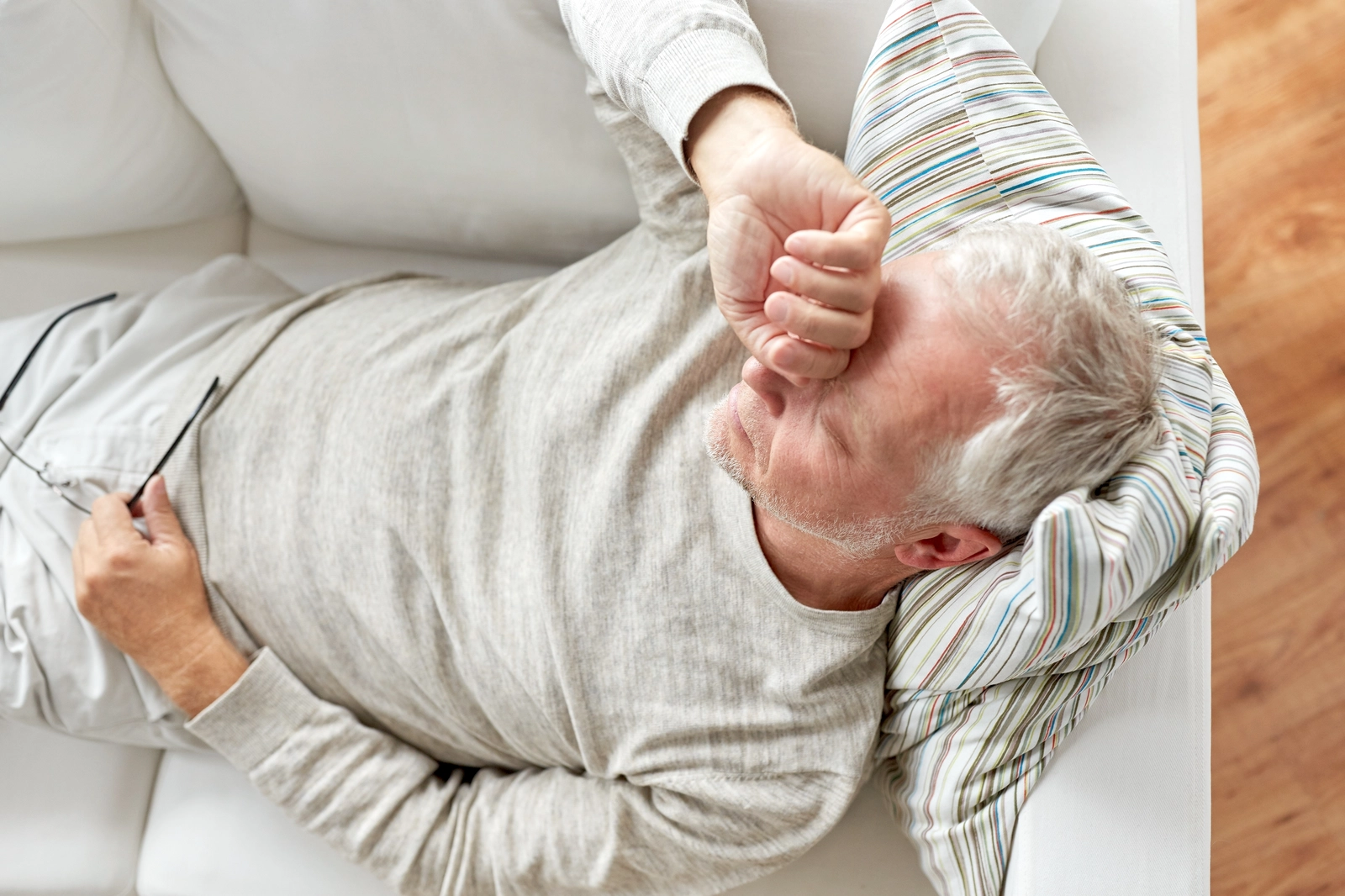 a man laying on the couch in pain rubs his forehead