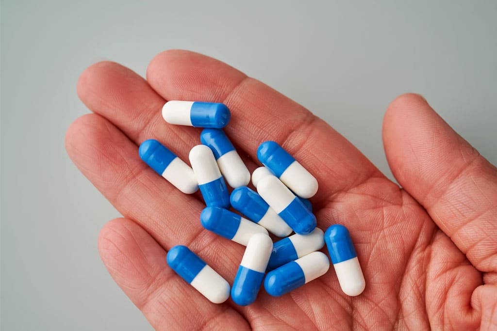 Blue and white pill capsules in the palm of someone's hand