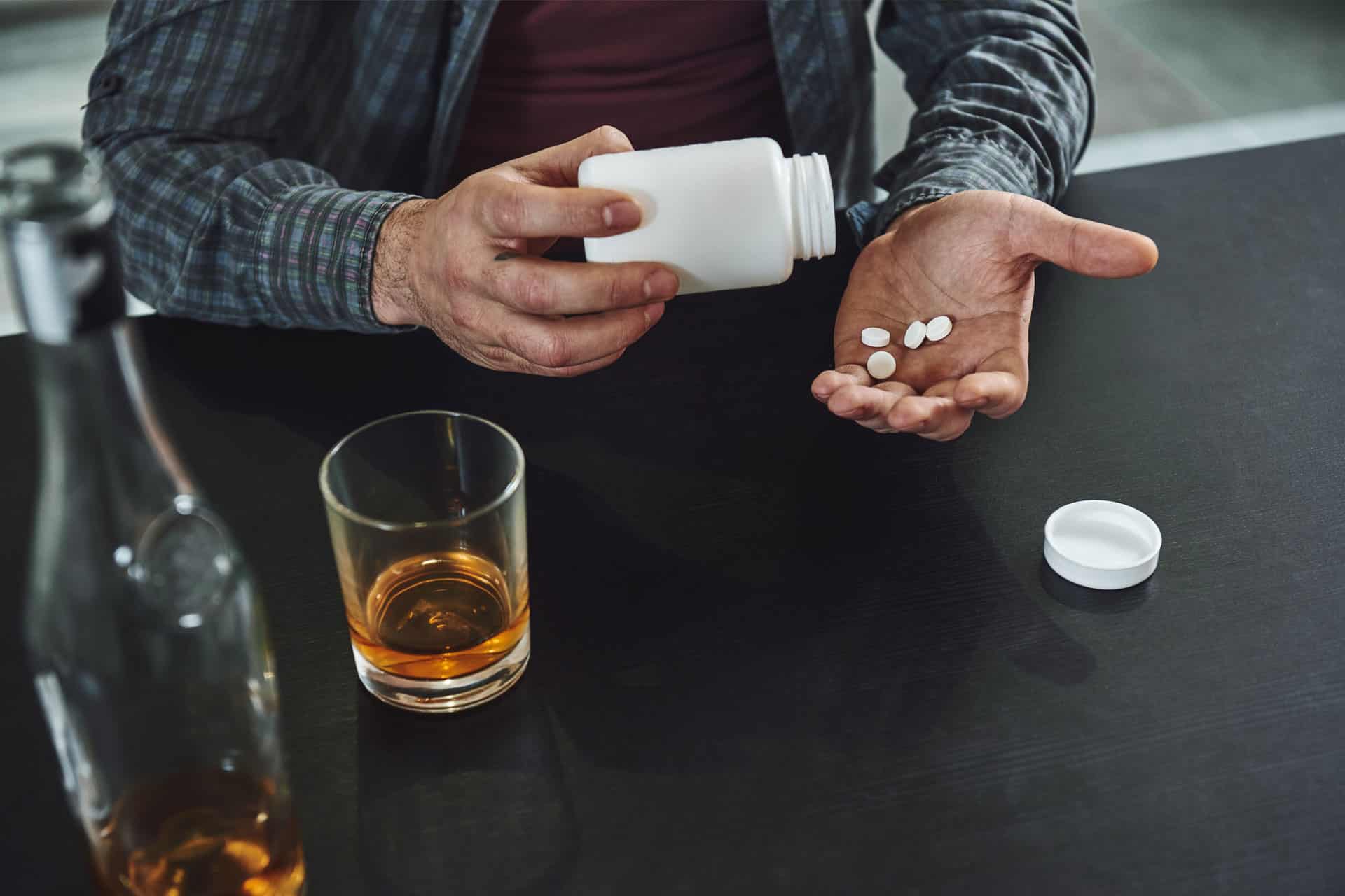 Trazodone and Alcohol: A person pouring pills into their hand, with a glass of alcohol on the table in front of them.