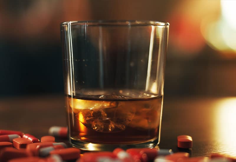 Trazodone-and-Alcohol: A glass of whiskey with pills all around it.